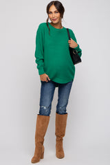 woman wearing a green oversized knitted maternity sweater with distressed jeans, paired with tan knee-high boots and a small bag