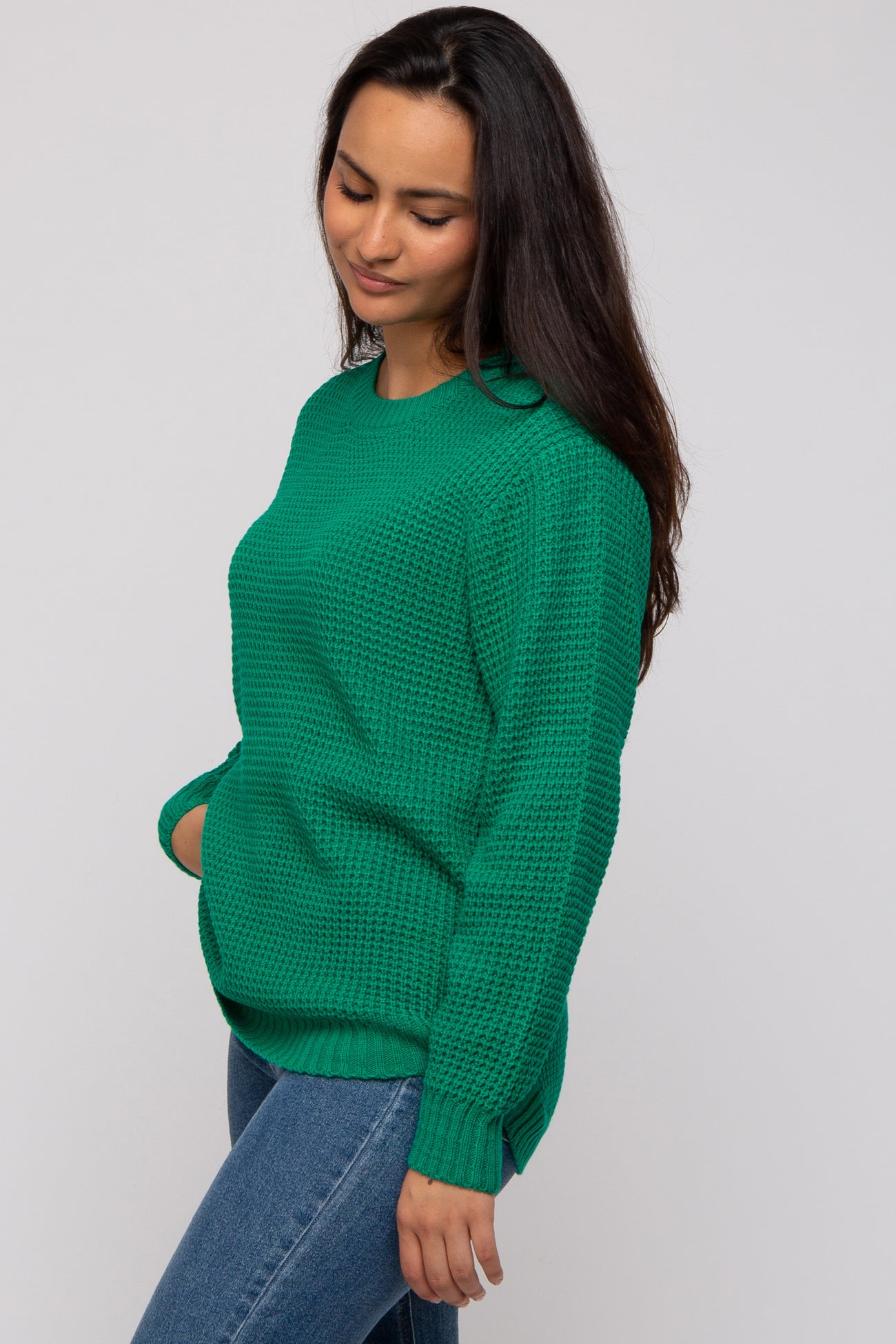 woman wearing a green oversized knit sweater with a textured pattern and side slits, paired with denim jeans