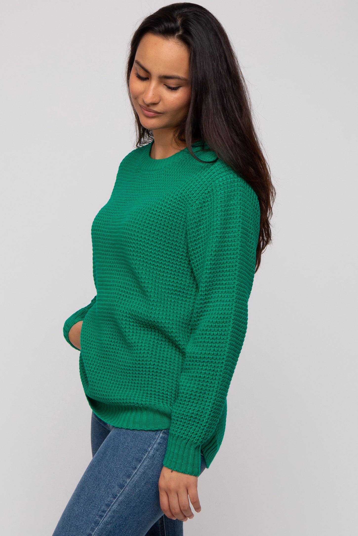 woman wearing a green oversized knit sweater with a textured pattern and side slits, paired with denim jeans