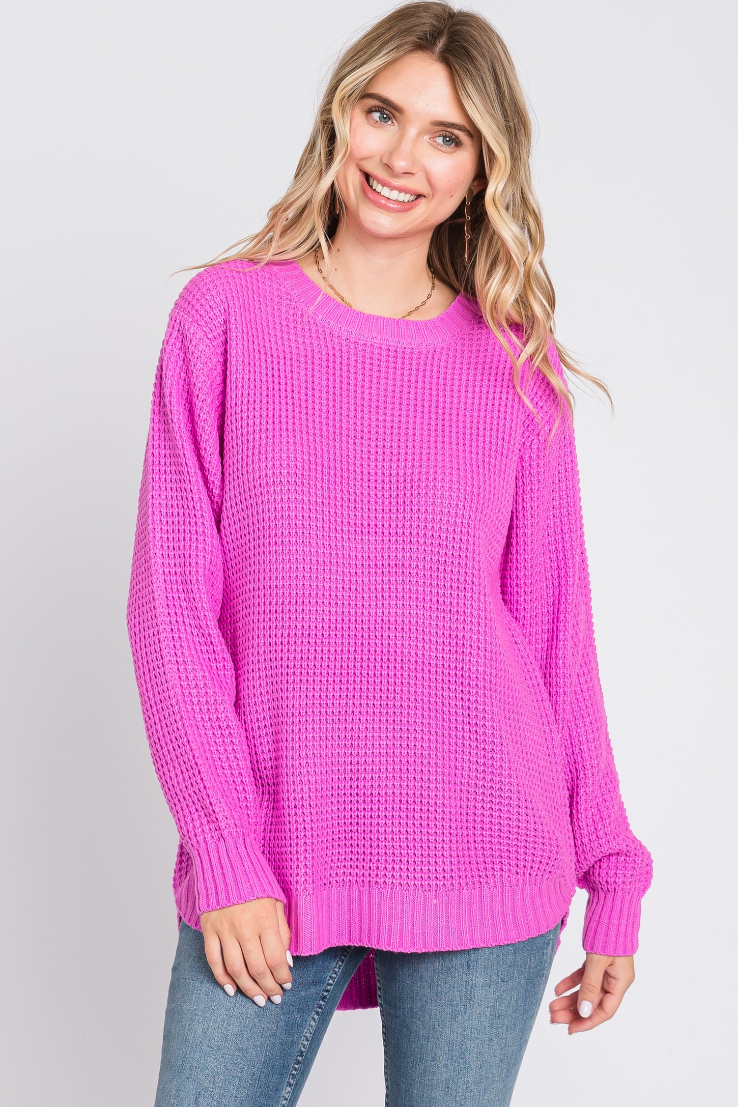 woman wearing a bright pink oversized knit sweater and blue jeans, smiling at the camera
