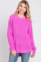 woman wearing a bright pink oversized knit sweater and blue jeans, smiling at the camera