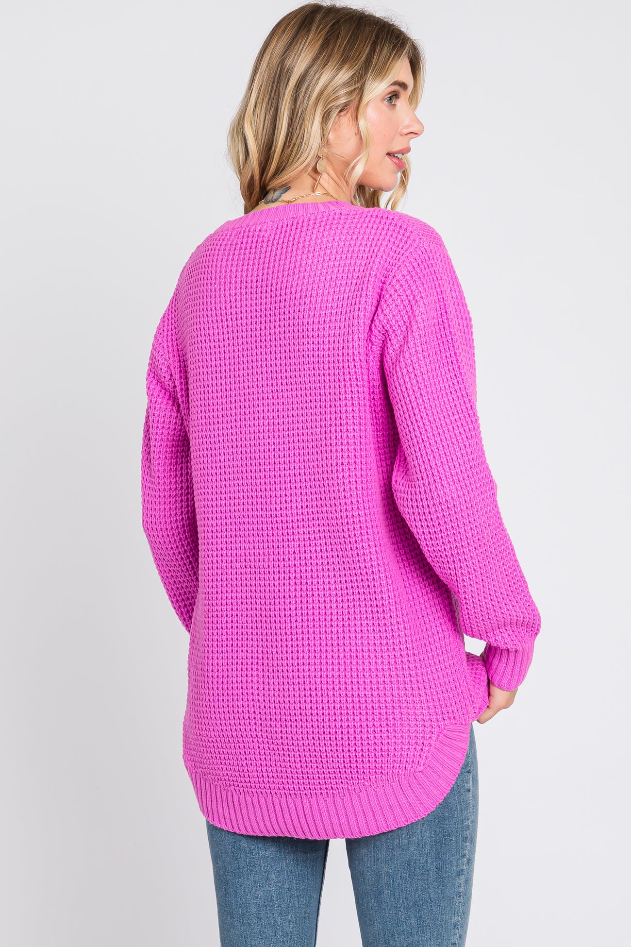 woman wearing a bright pink chunky knit sweater with a slightly longer back and relaxed fit, paired with jeans