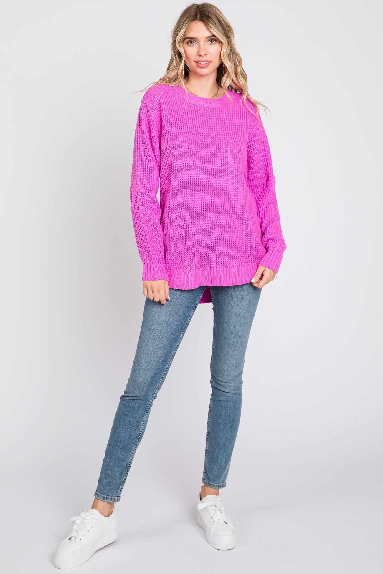 woman wearing a bright pink oversized knit sweater and light blue skinny jeans with white sneakers