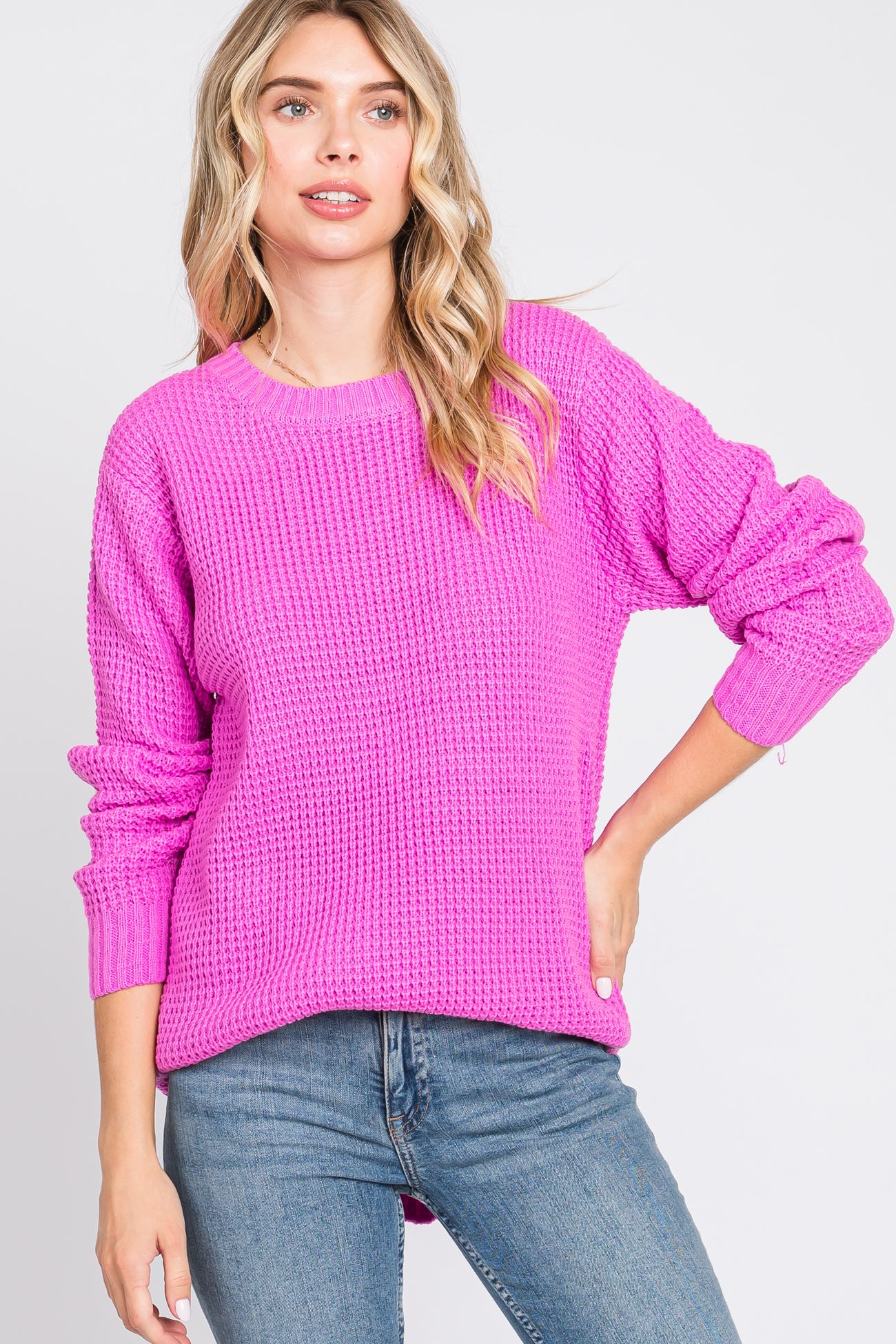woman wearing a bright pink knit sweater with long sleeves and a relaxed fit, paired with blue jeans