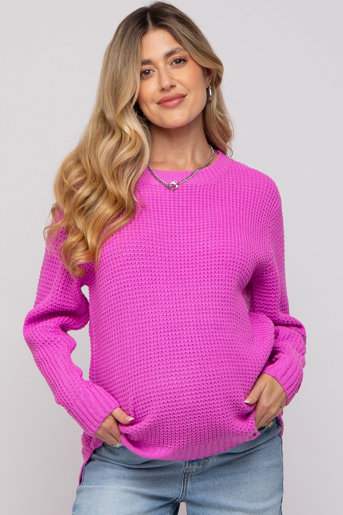 woman wearing a bright pink maternity sweater with a textured knit and side slits, holding her baby bump