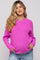 woman wearing a bright pink maternity sweater with a textured knit and side slits, holding her baby bump