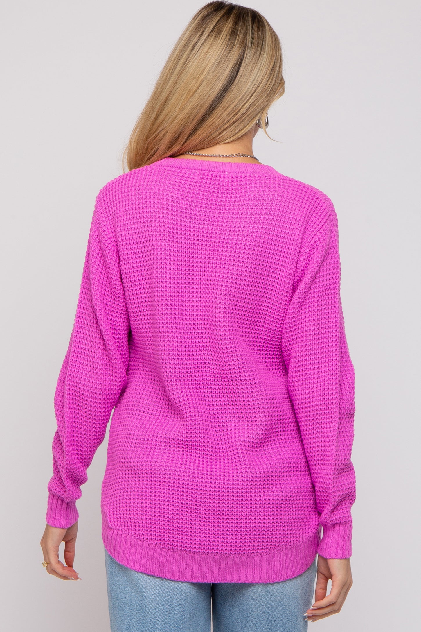 woman wearing a bright pink long sleeve knitted maternity sweater, shown from the back