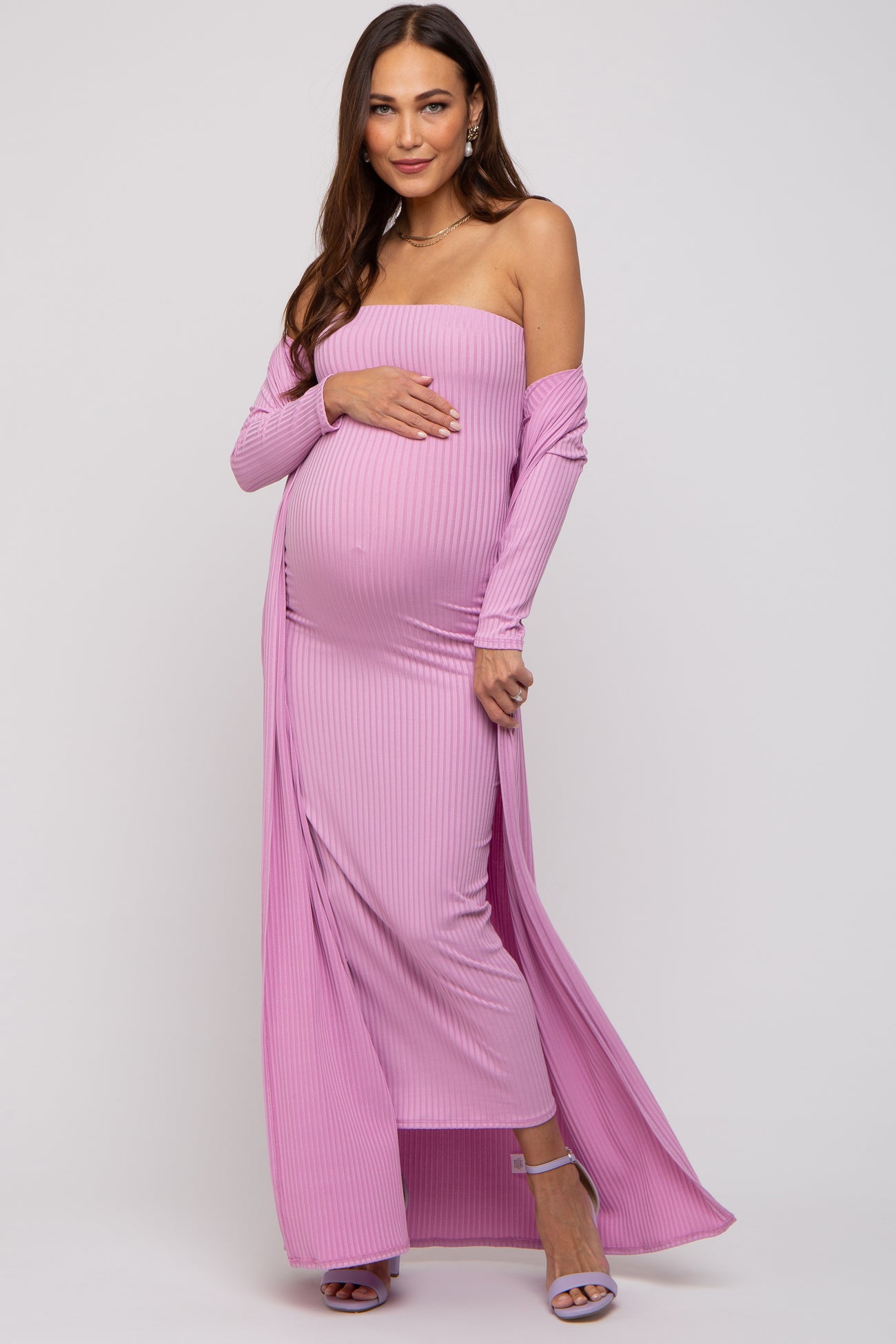 woman wearing a pink off-shoulder maternity gown with long sleeves and a side slit, showcasing her baby bump