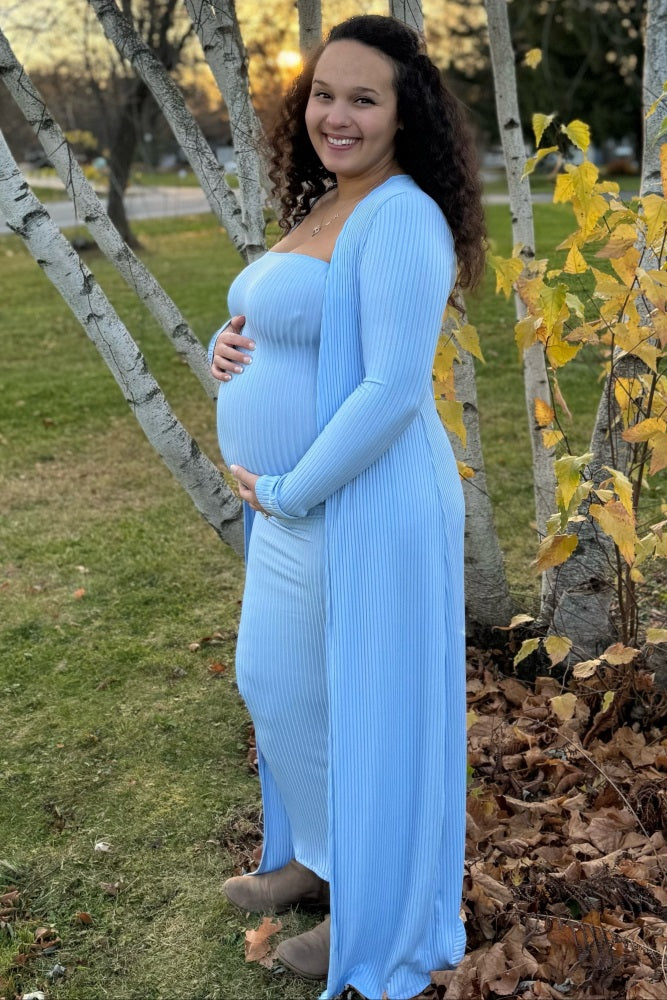 woman wearing a light blue maternity maxi dress with a matching cardigan, showing her baby bump while standing outdoors
