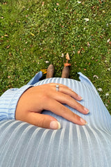 woman wearing a light blue striped maternity top with a visible baby bump, hand resting on her belly