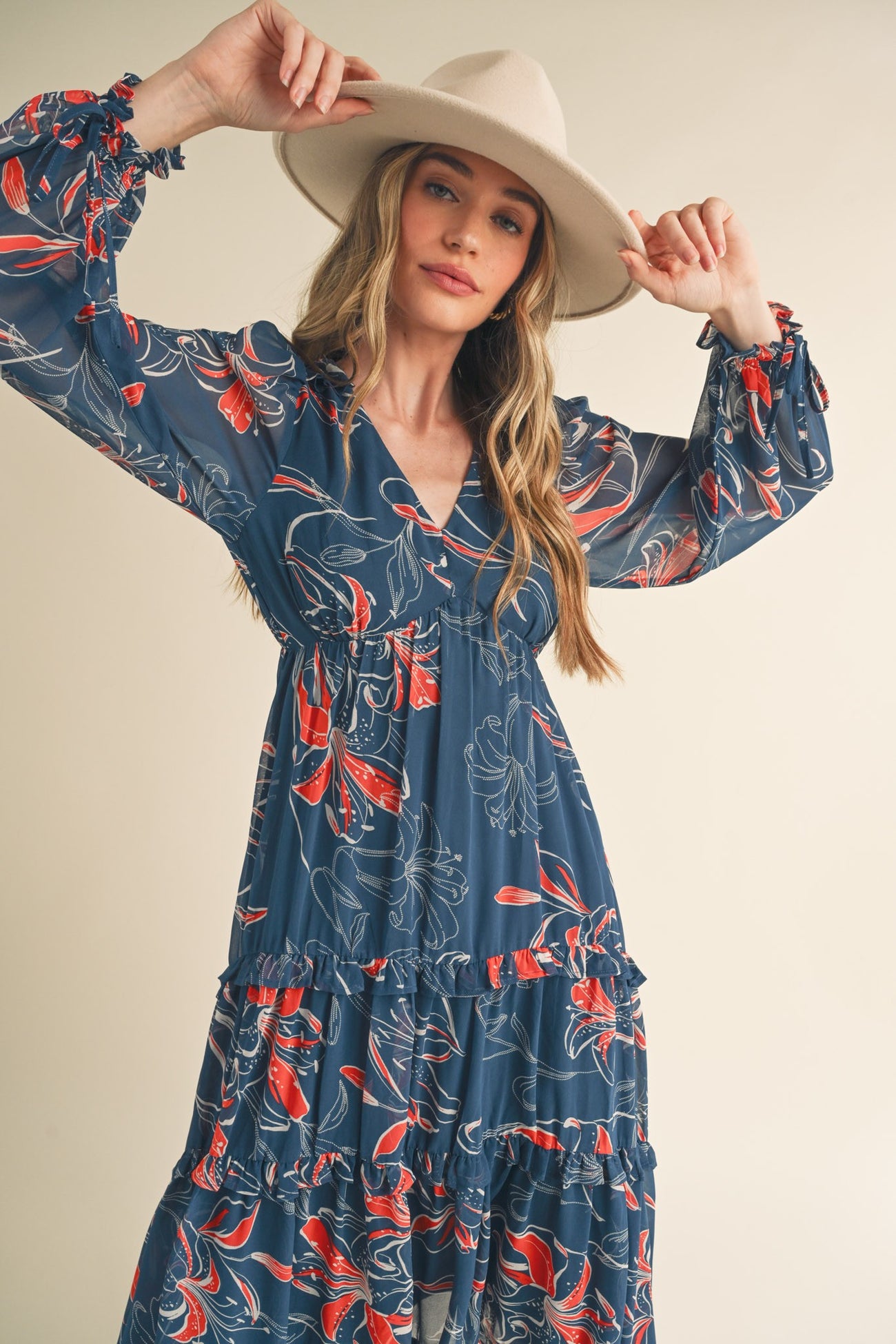 woman wearing a flowy navy blue floral maxi dress with ruffles and long sleeves, holding a hat
