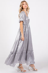 woman wearing a shimmering silver maxi dress with puff sleeves and ruffled hem, styled with strappy white heels