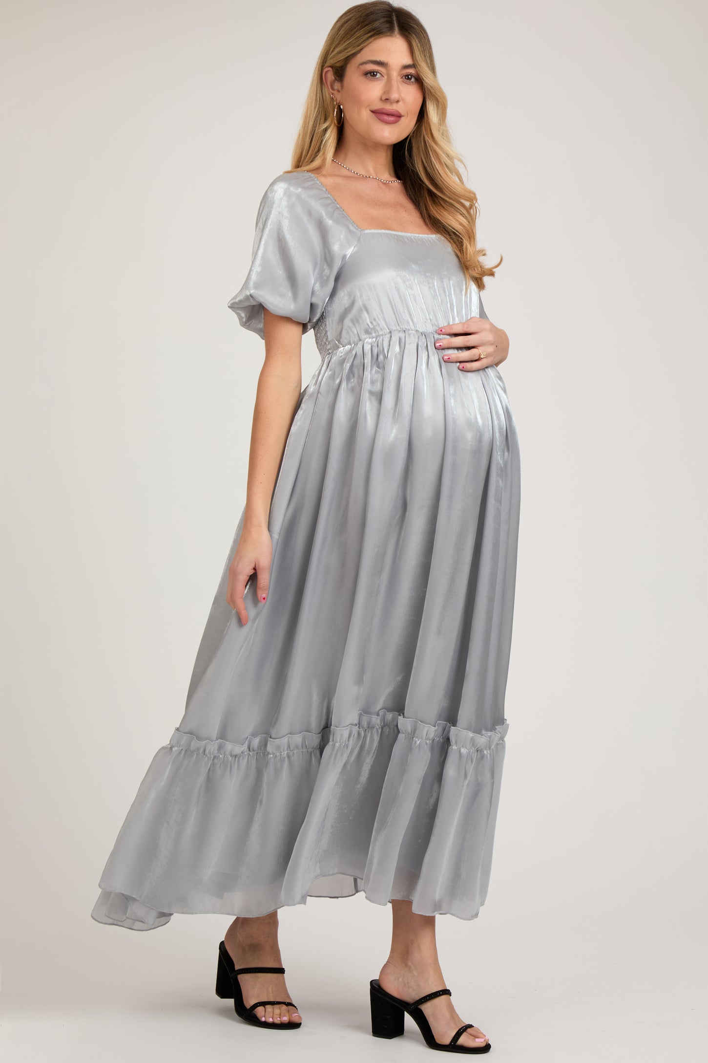 woman wearing a silver maternity maxi dress with puff sleeves and a tiered ruffled hem, showing her baby bump