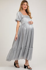 woman wearing a silver maternity maxi dress with puff sleeves and a tiered ruffled hem, showing her baby bump