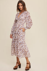woman wearing a light purple floral maxi dress with long sleeves and ruffled neckline, standing in a neutral background