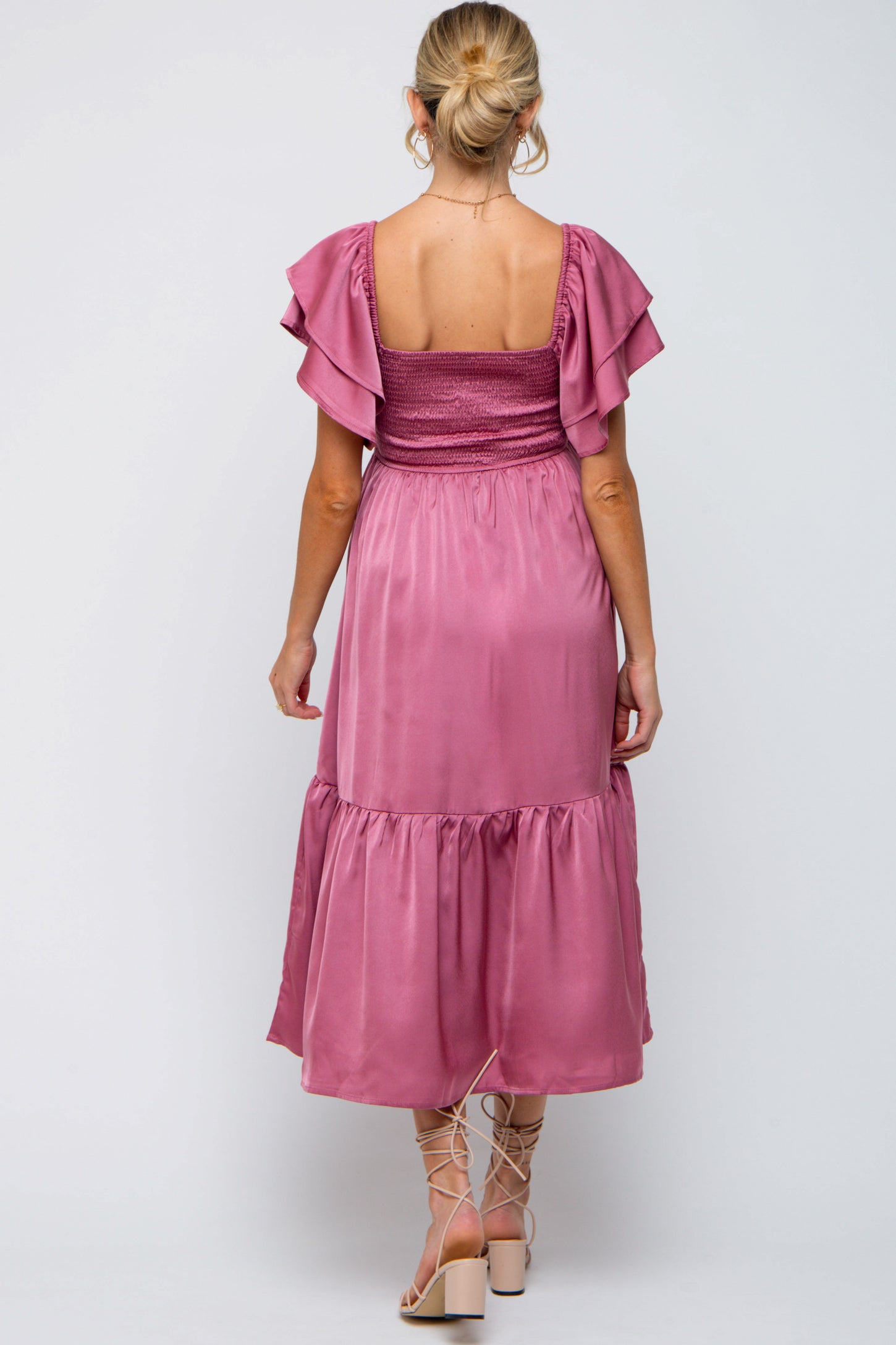 woman wearing a mauve maternity dress with ruffled sleeves and a tiered skirt, showing a baby bump from the back