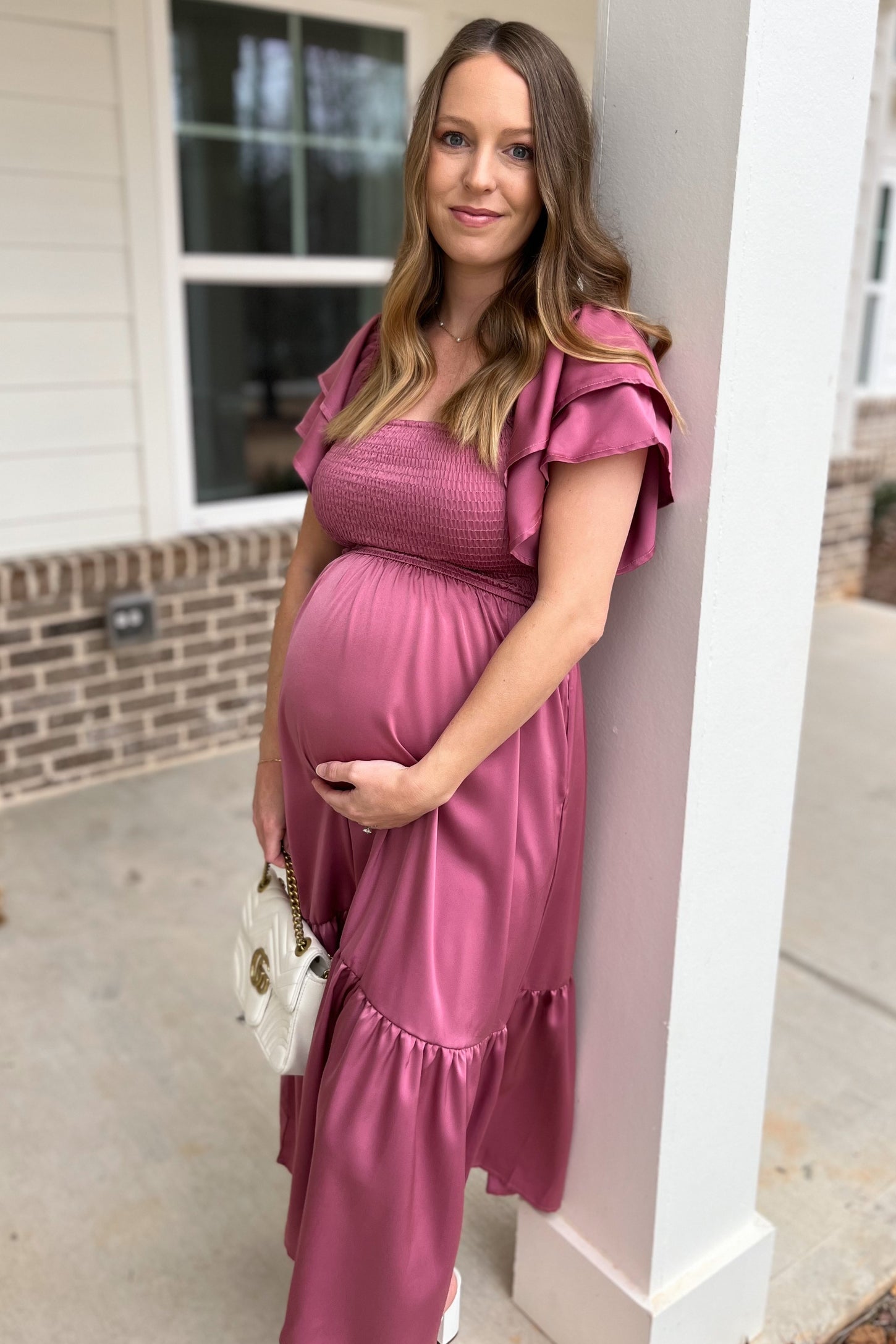 woman wearing a dusty pink maternity dress with ruffle sleeves and holding her baby bump