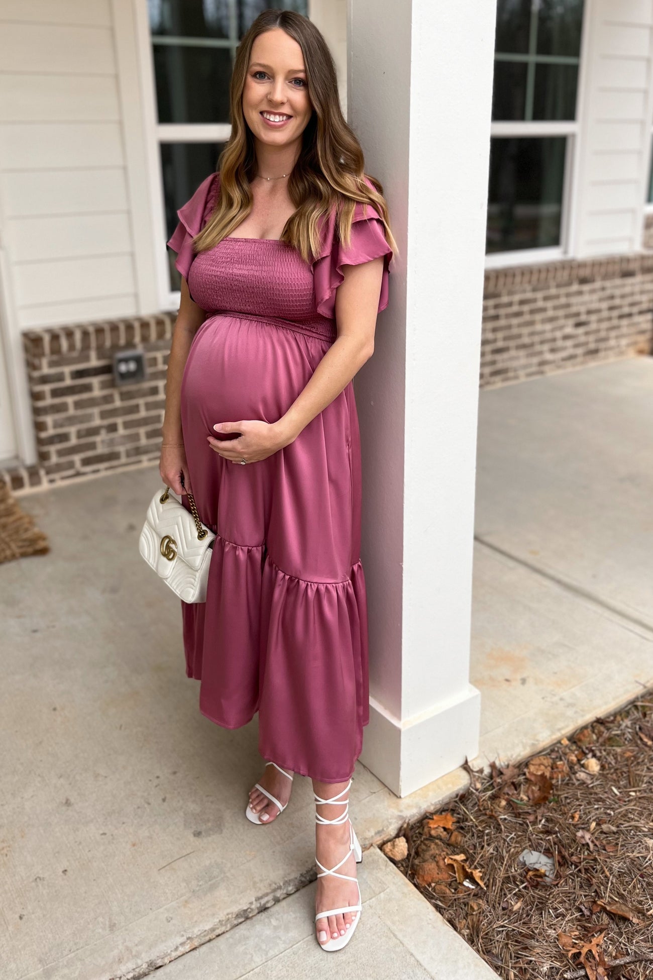 woman wearing a dusty pink maternity dress with ruffle sleeves and a baby bump, holding a white handbag