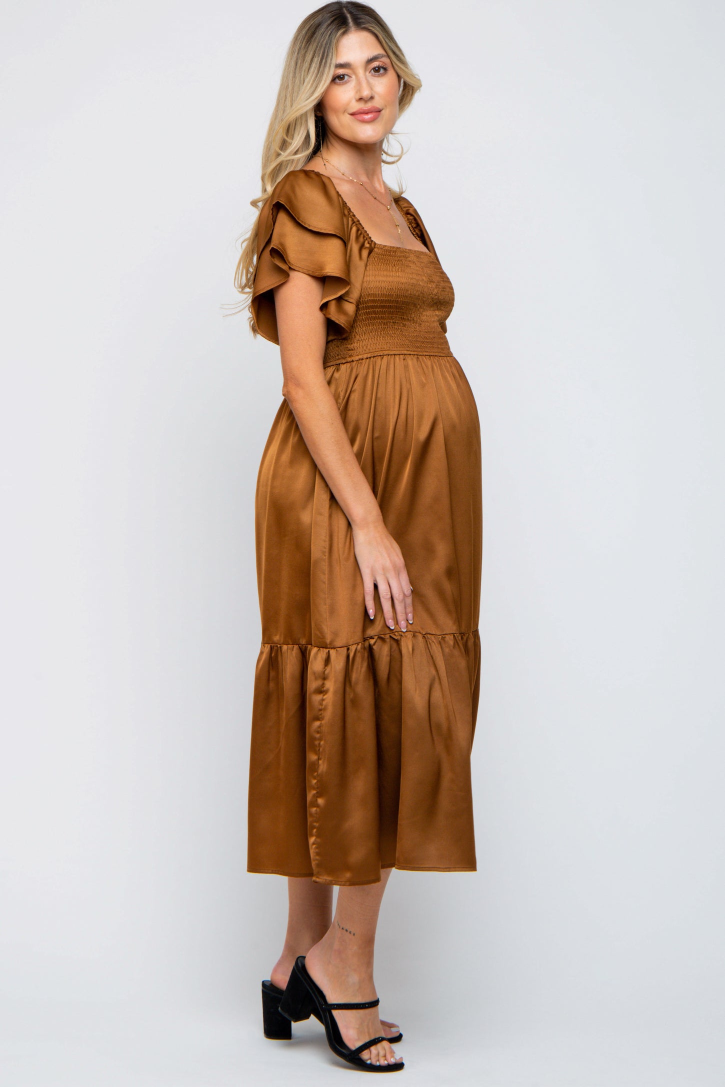 woman wearing a rust-colored maternity dress with flutter sleeves and a smocked bodice, showcasing her baby bump
