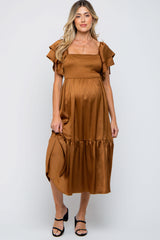 woman wearing a brown maternity dress with ruffled sleeves and a smocked bodice, posing with a visible baby bump
