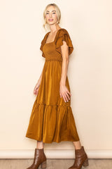 woman wearing a rust-colored smocked maxi dress with ruffled sleeves and a tiered skirt, paired with brown ankle boots