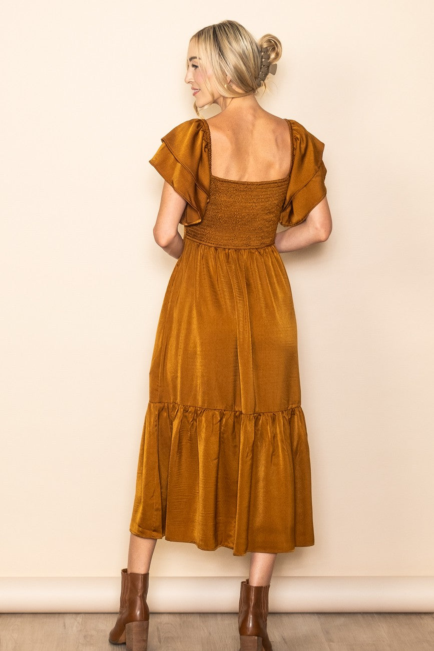 woman wearing a mustard yellow midi dress with flutter sleeves and a smocked bodice, standing with her back to the camera