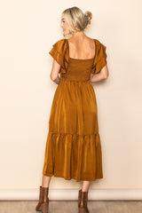 woman wearing a mustard yellow midi dress with flutter sleeves and a smocked bodice, standing with her back to the camera