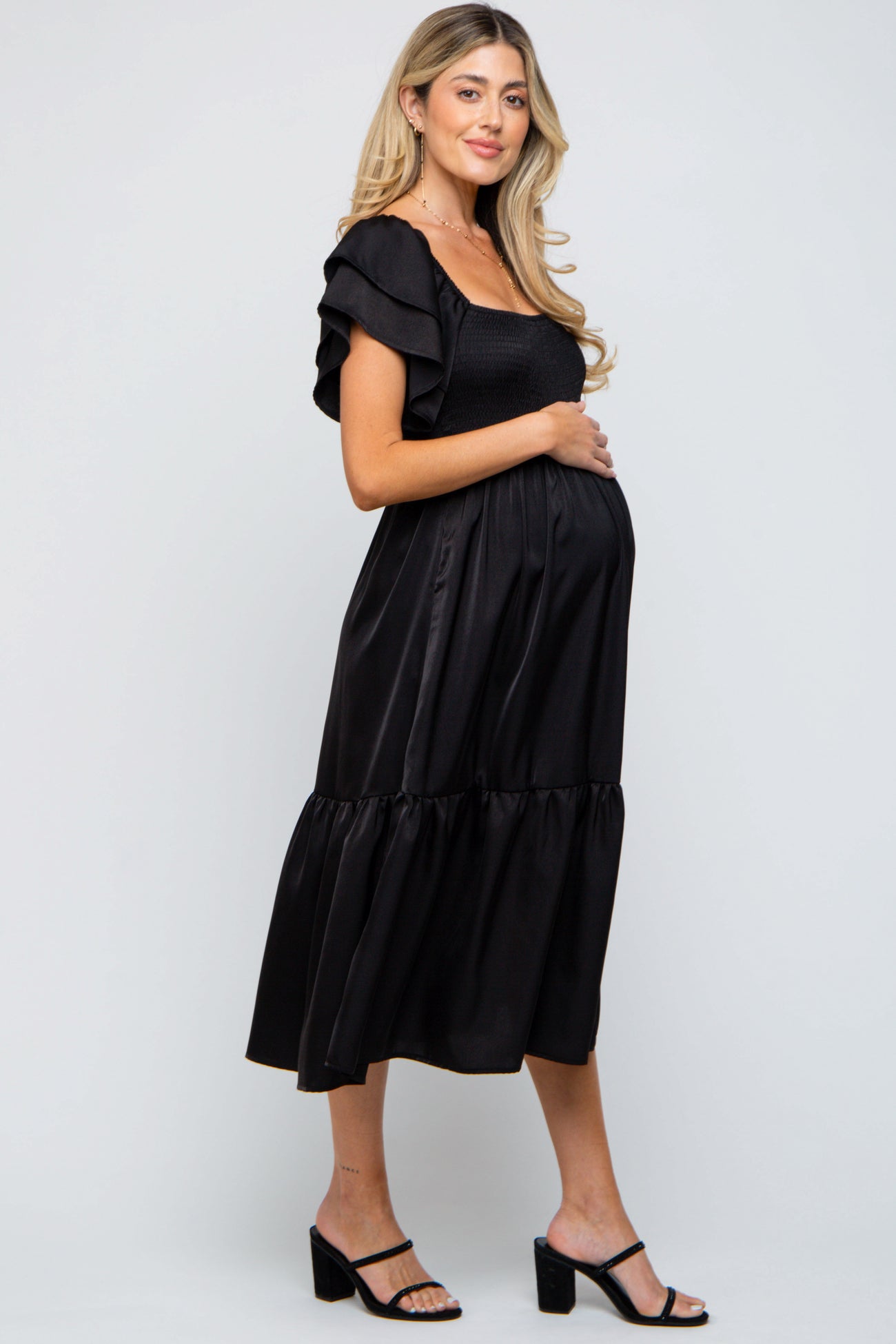 woman wearing a black maternity dress with ruffled sleeves and a tiered hem, posing with a visible baby bump