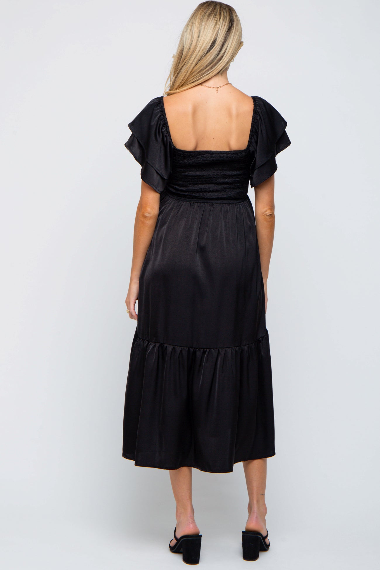 woman wearing a black maternity dress with ruffled sleeves and a tiered skirt, view from the back