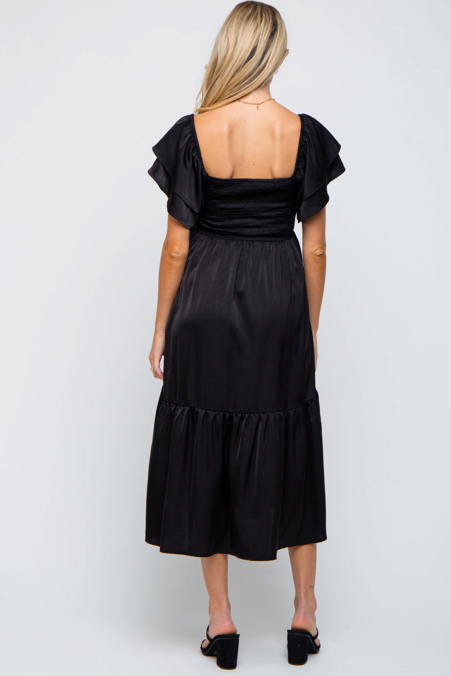 woman wearing a black maternity dress with ruffled sleeves and a tiered skirt, view from the back