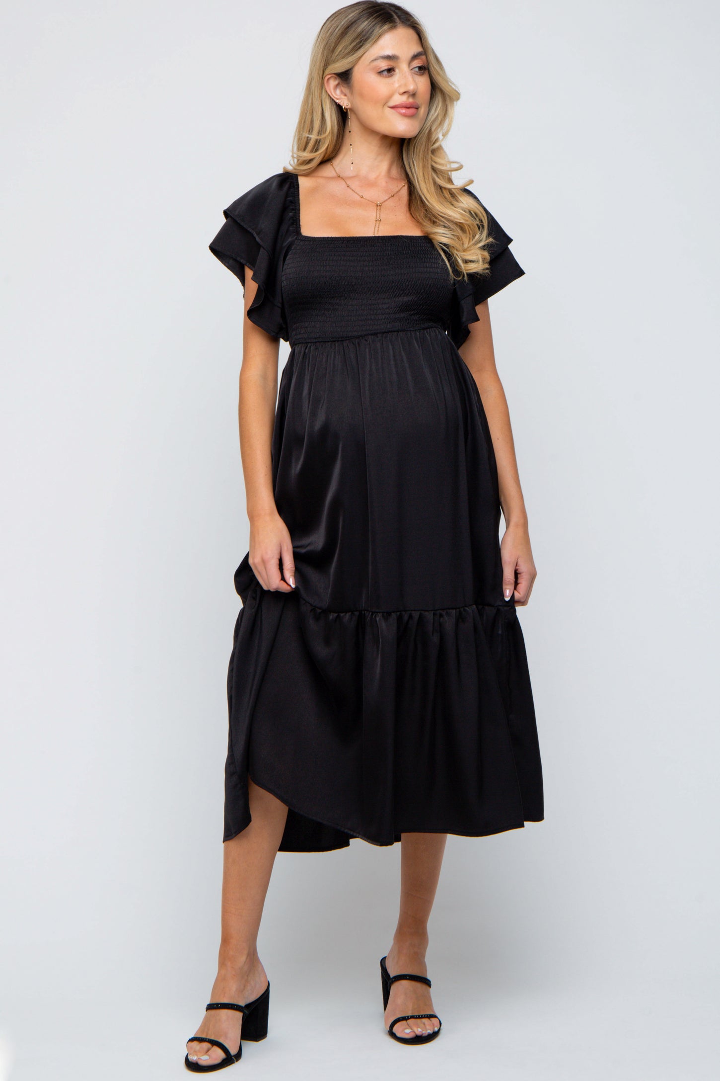 woman wearing a black maternity dress with ruffled sleeves and a tiered hem, displaying her baby bump