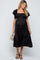 woman wearing a black maternity dress with smocked bodice and ruffle sleeves, holding a small bag and showing baby bump