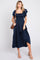 woman wearing a navy blue smocked maxi dress with ruffled sleeves, holding a brown handbag and wearing nude heeled sandals