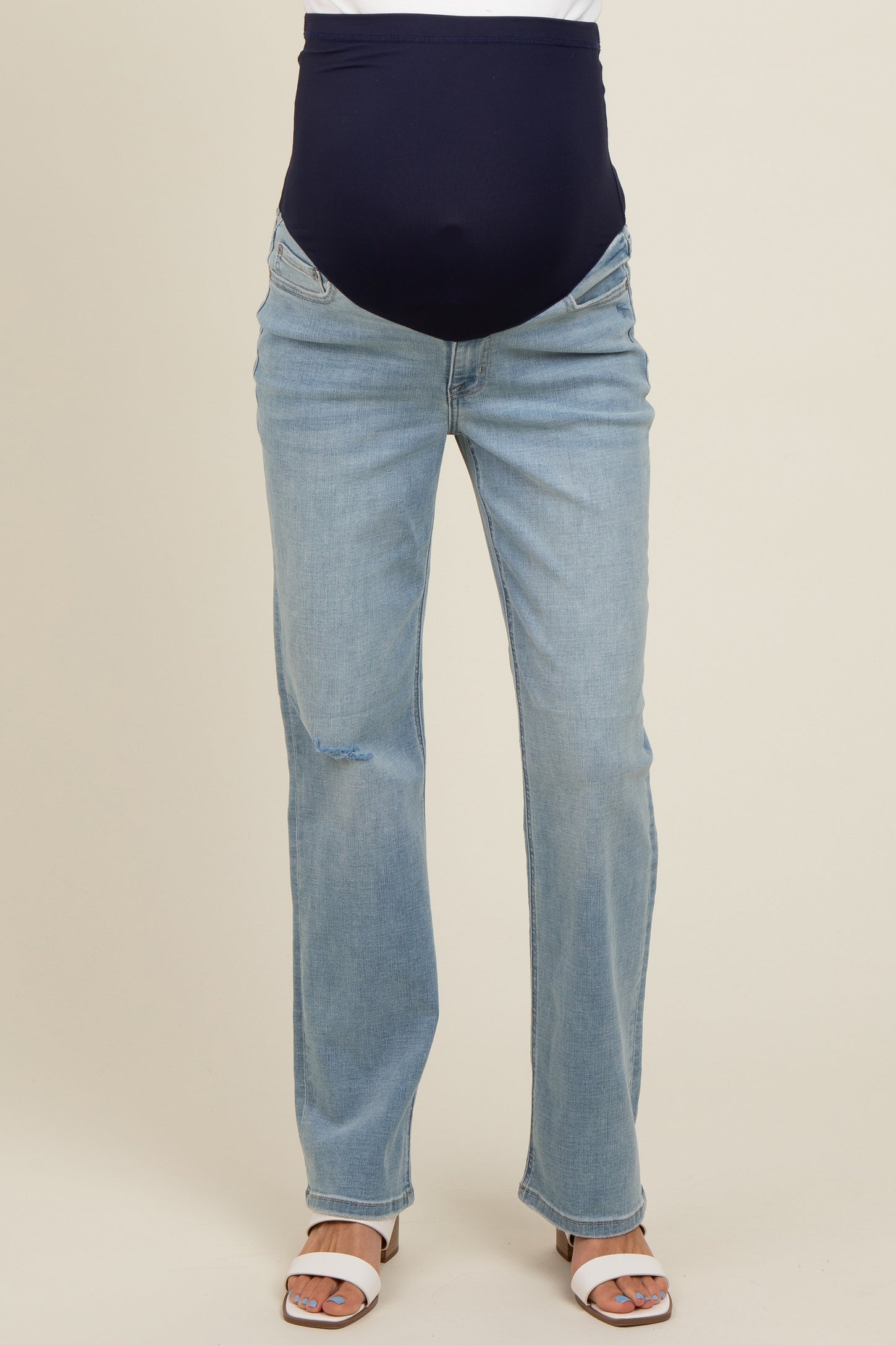 woman wearing a pair of light wash maternity jeans with a dark blue belly band and open-toe sandals