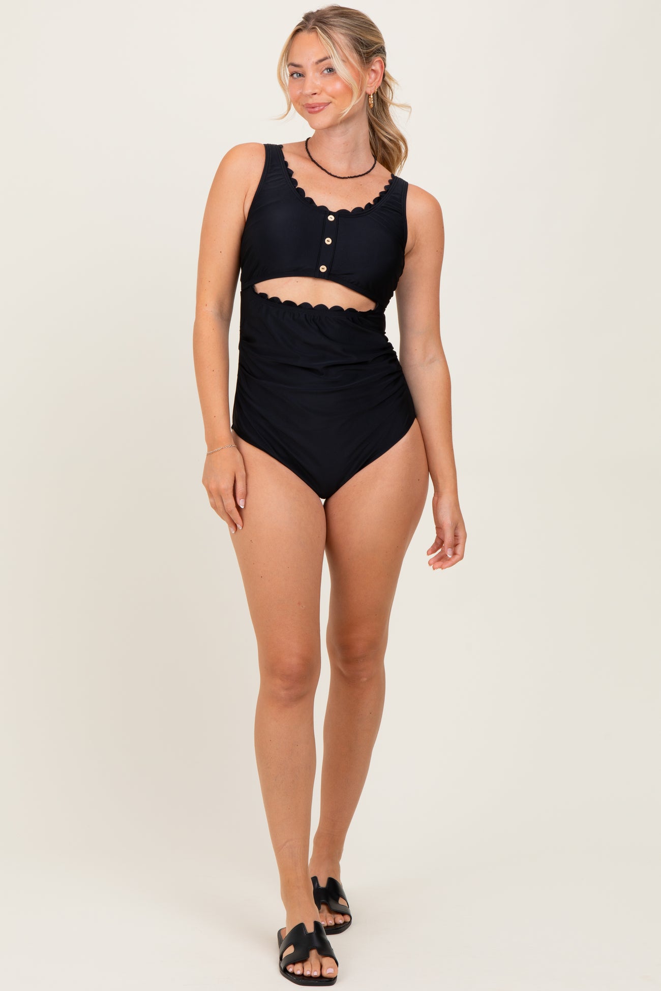 woman wearing a black two-piece swimsuit with scalloped details and a high-waisted bottom, standing and smiling