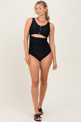 woman wearing a black two-piece swimsuit with scalloped details and a high-waisted bottom, standing and smiling