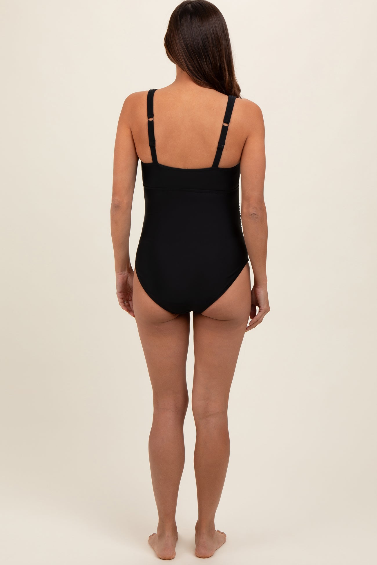 woman wearing a black maternity swimsuit, viewed from the back, featuring adjustable straps