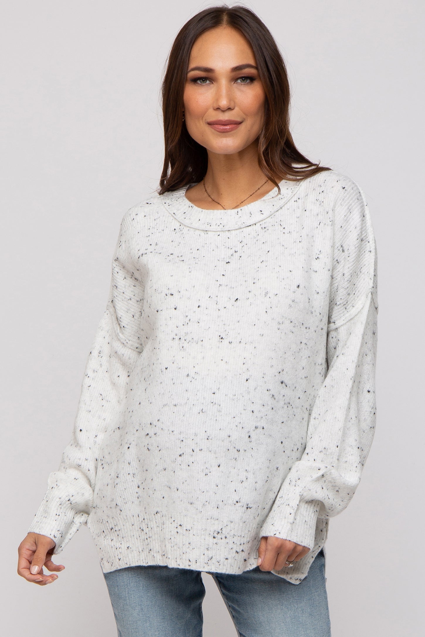 woman wearing a light grey speckled maternity sweater with a relaxed fit and long sleeves, showing her baby bump