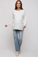woman wearing a white speckled maternity sweater with long sleeves and paired with distressed light blue jeans