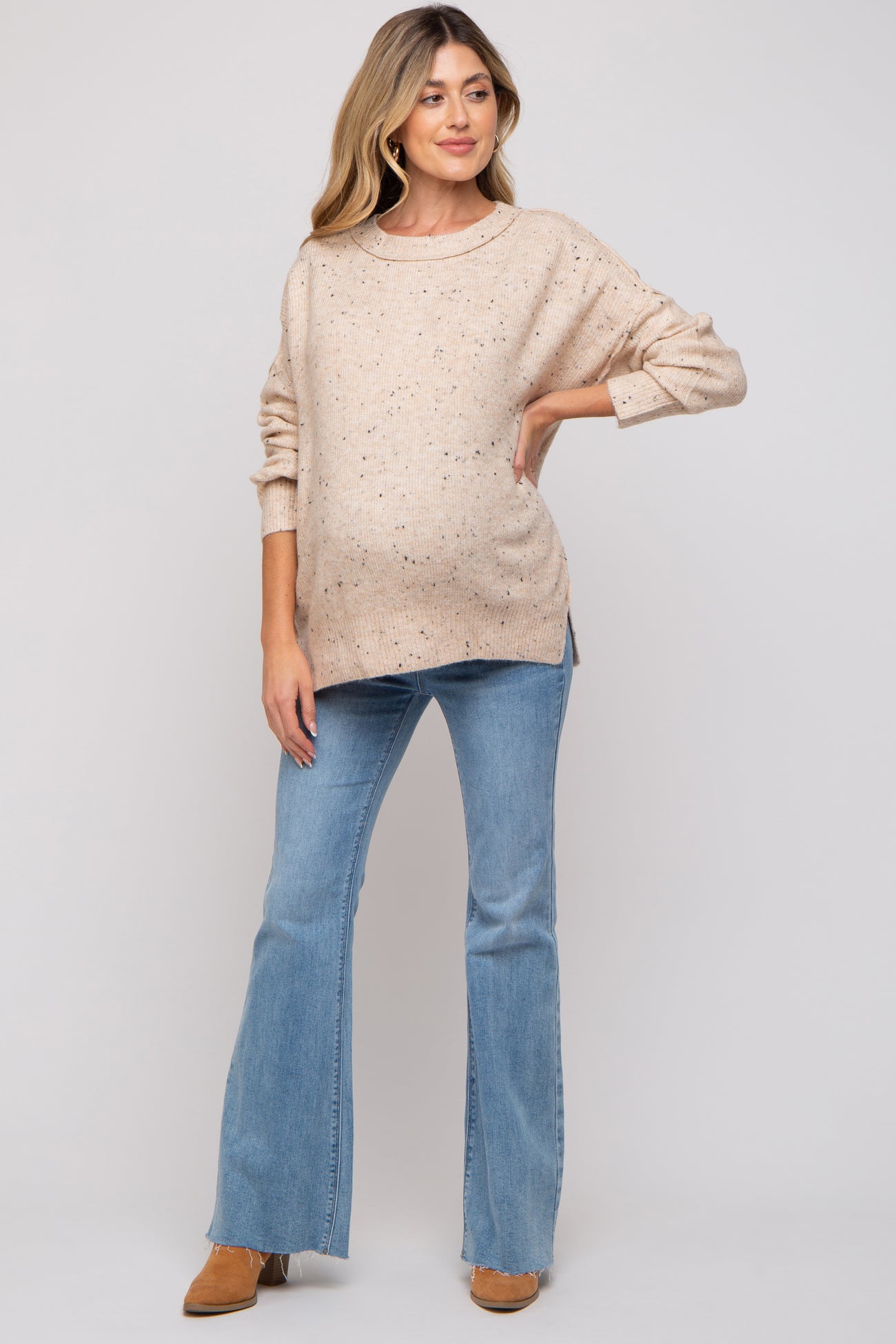 woman wearing a beige speckled maternity sweater and light blue flared jeans with a visible baby bump