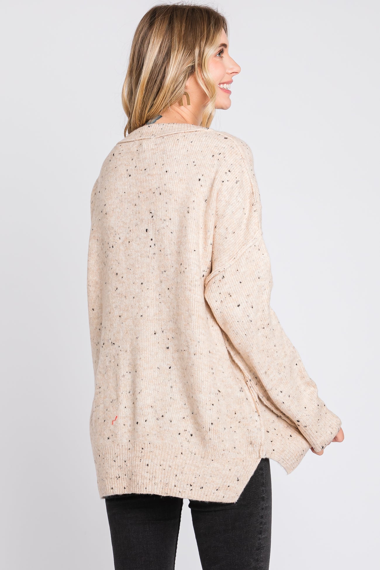 woman wearing a beige speckled oversized knit sweater, viewed from the back, with black skinny jeans