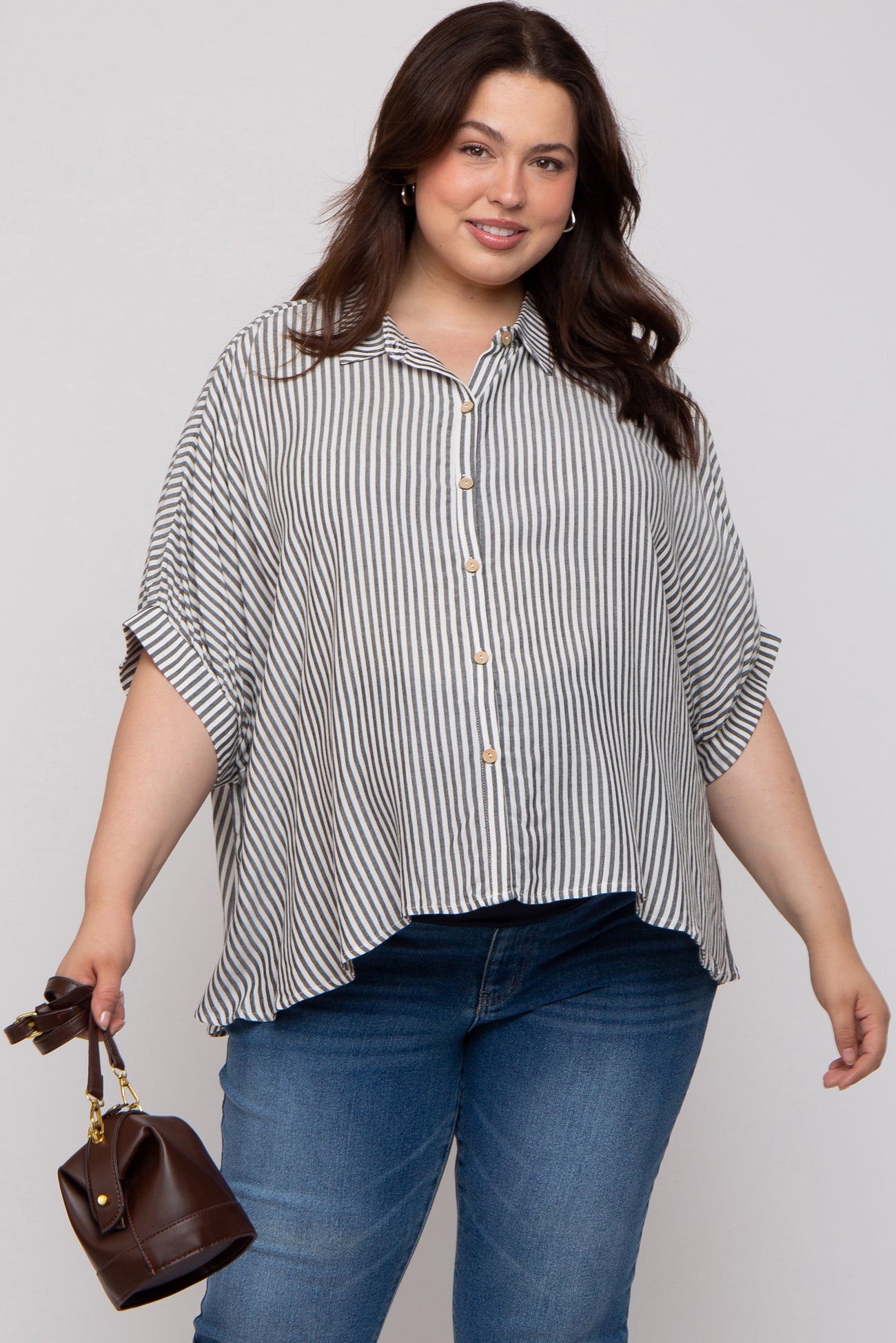 woman wearing a black and white striped maternity plus button-up blouse with rolled sleeves, holding a small handbag