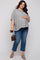 woman wearing a black and white striped maternity top and holding her baby bump with blue cropped jeans and a brown handbag