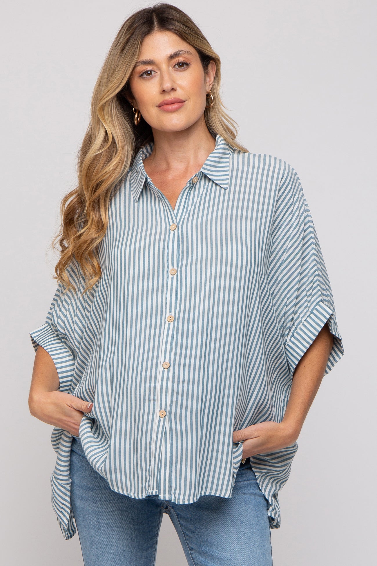 woman wearing a light blue and white striped maternity shirt with a loose fit and short sleeves, hands in pockets