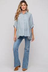 woman wearing a light blue striped button-up maternity shirt and flared jeans, displaying her baby bump