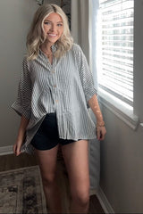 woman wearing a striped oversized button-up shirt with rolled sleeves, styled with black shorts and no visible baby bump