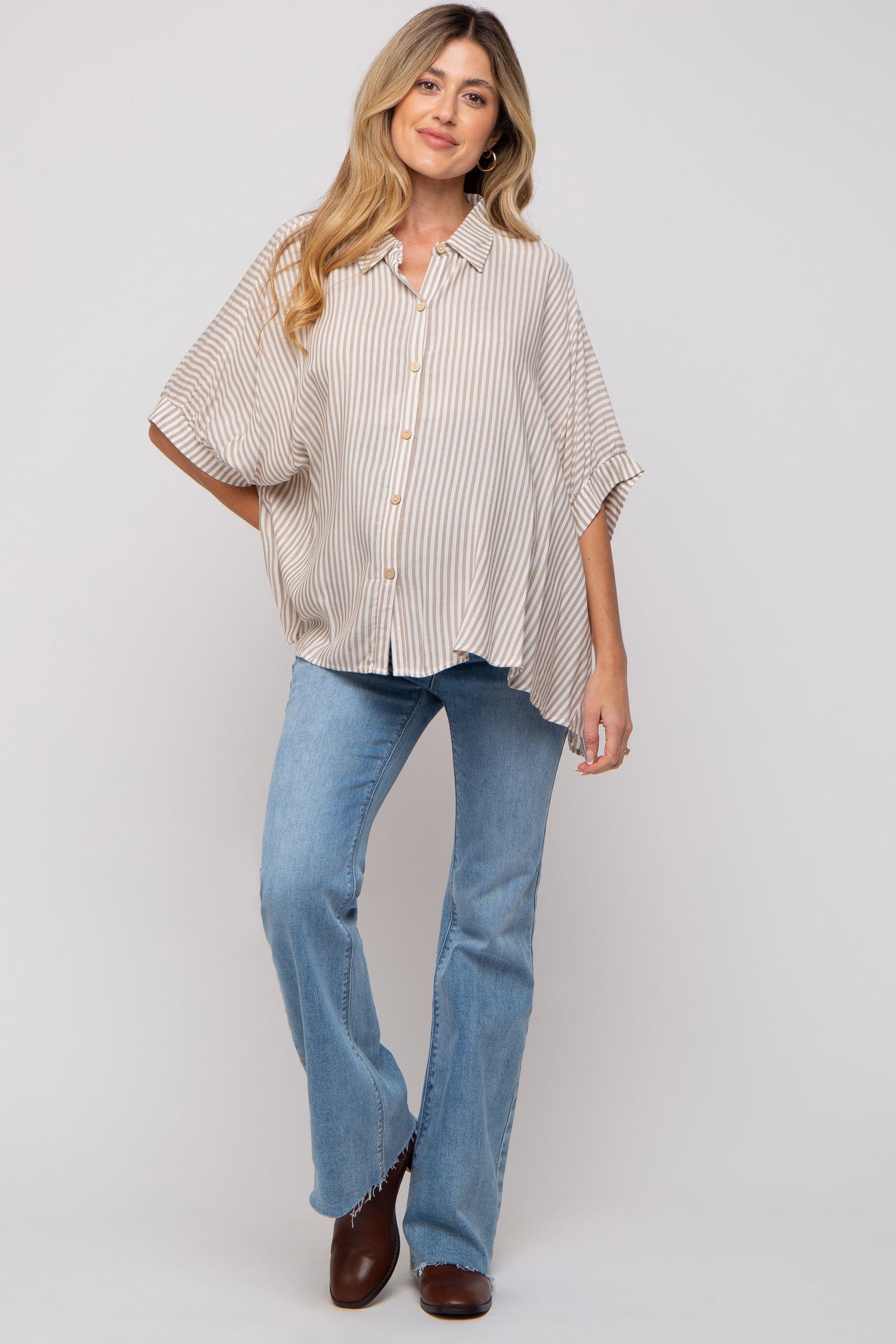 woman wearing a light beige and white striped maternity top with short sleeves and buttons, paired with flared jeans and brown boots