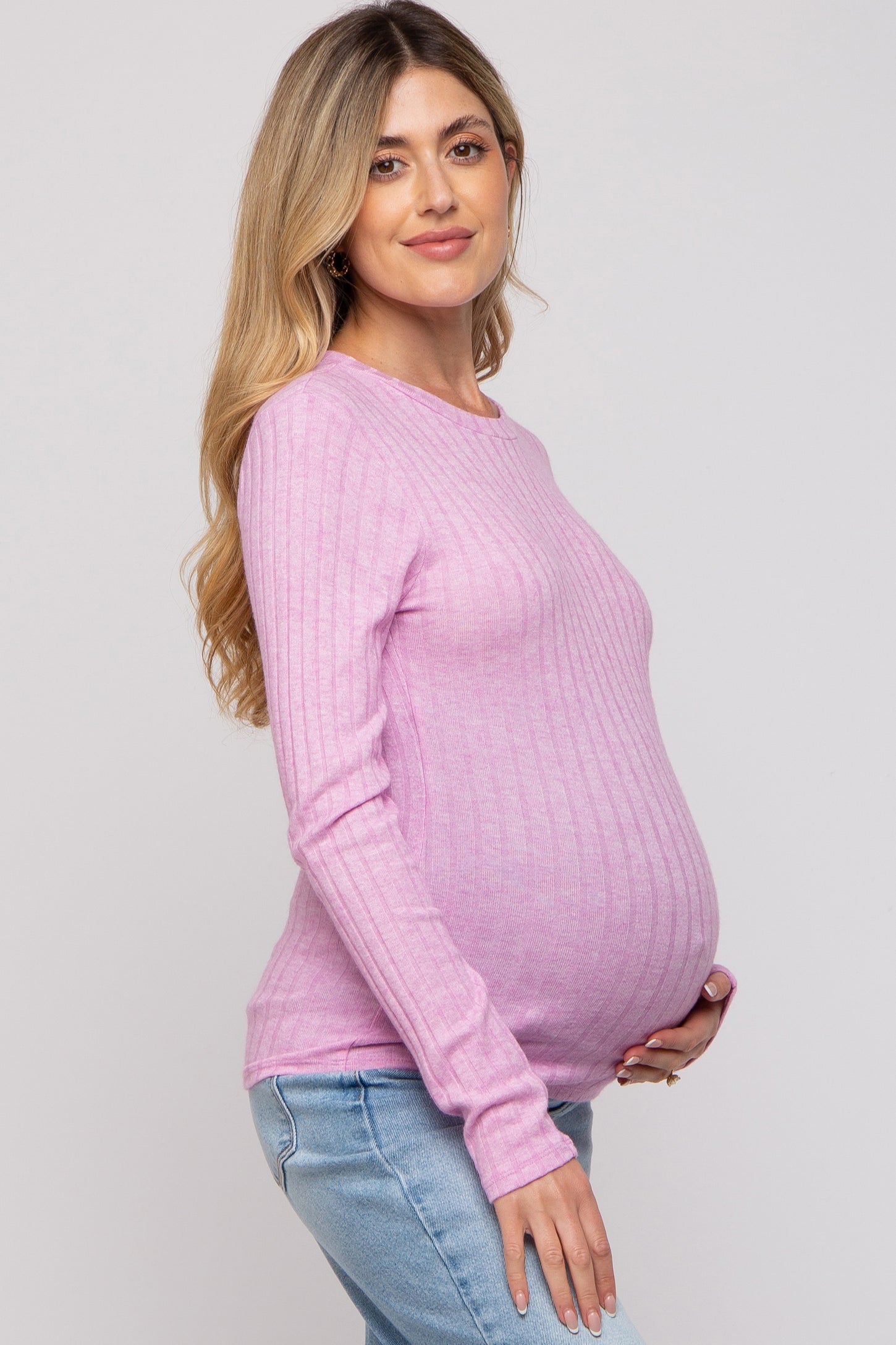 woman wearing a pink ribbed long sleeve maternity top and holding her baby bump