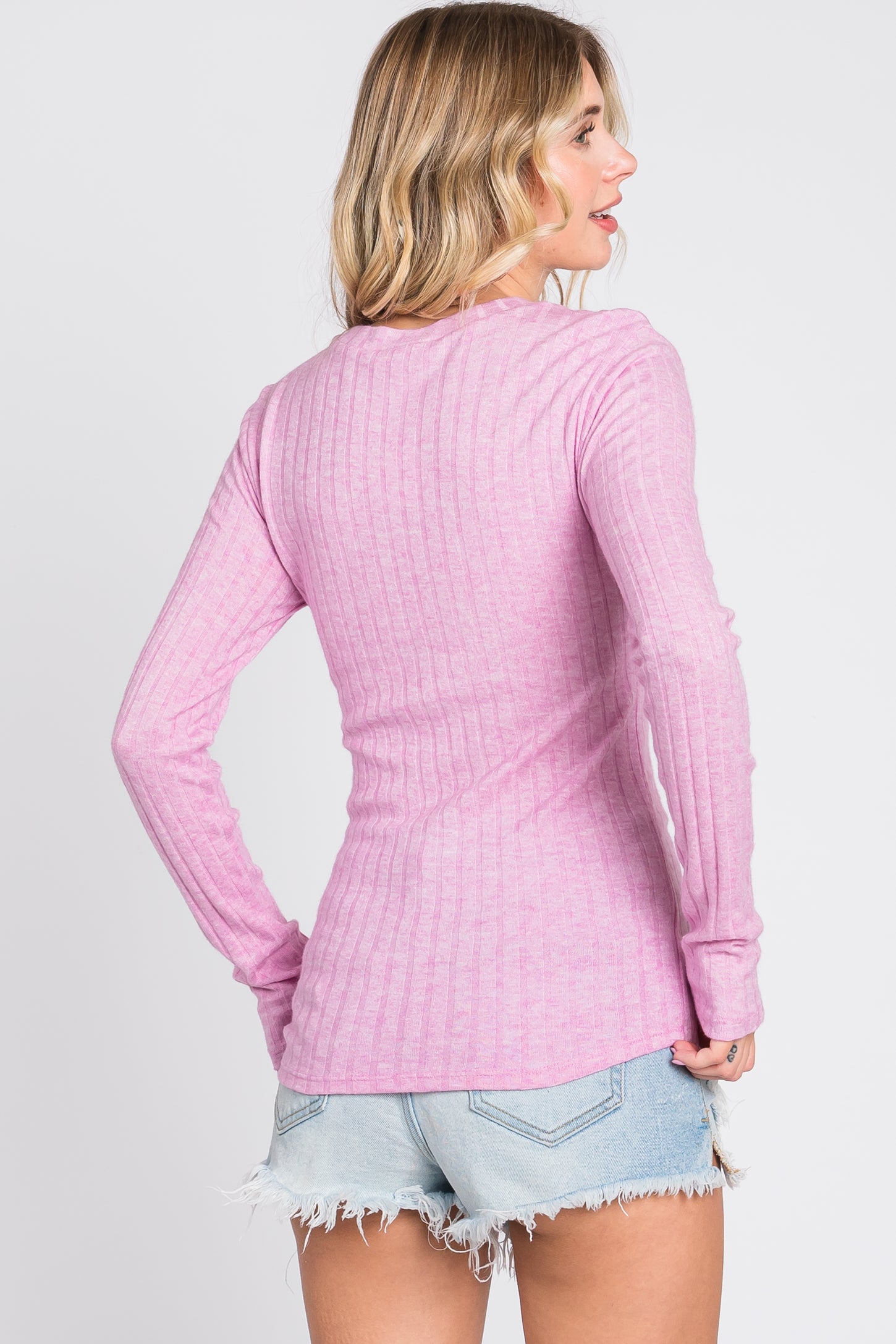 woman wearing a light pink ribbed long sleeve top with a relaxed fit and styled with distressed denim shorts
