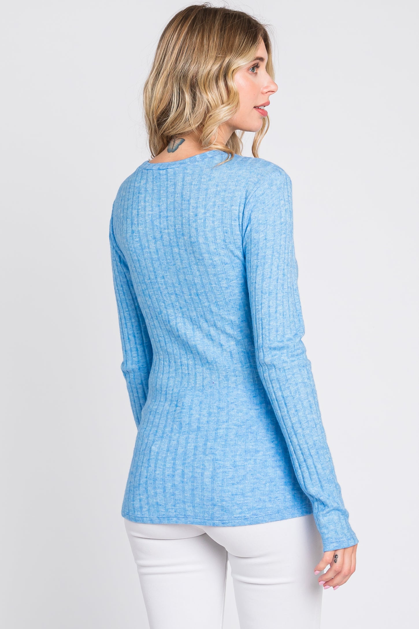 woman wearing a light blue ribbed long sleeve top with a fitted silhouette and slightly longer back hem